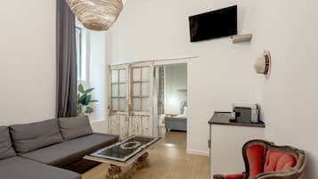 Een moderne woonkamer met een bank, een salontafel met glazen blad, een rode fauteuil, een televisie en een schuifdeur die naar een andere kamer leidt.