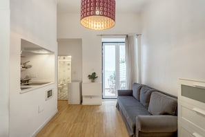 Ein modernes Wohnzimmer mit einer Couch, einem Essbereich mit Tisch und Stühlen, einer Küche mit Spüle und Herd sowie einer Schiebetür zu einem Balkon.
