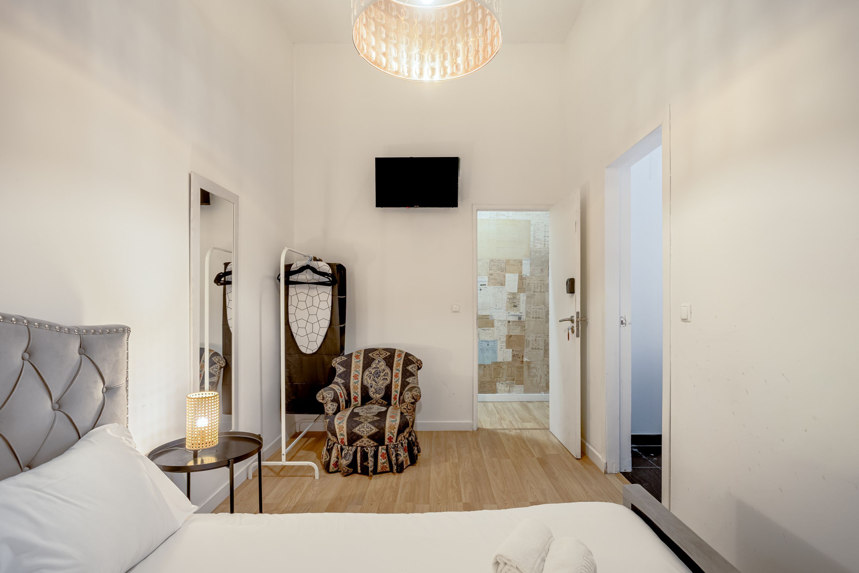 Une chambre à coucher comprenant un lit, une chaise, un téléviseur et une porte donnant sur une autre pièce.