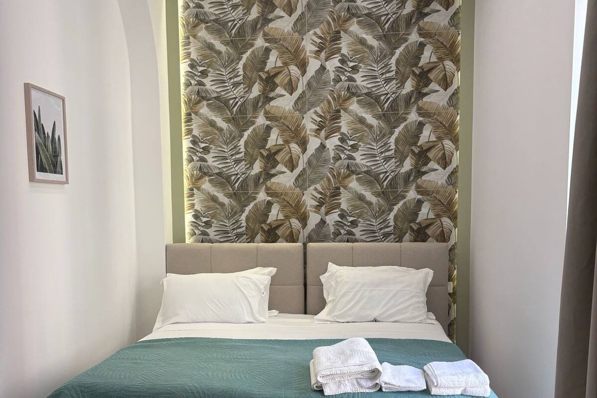 Ein Doppelbett mit grüner Bettdecke, zwei weißen Kissen und einem Kopfteil mit Blättermotiv.