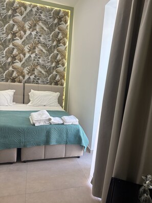 A hotel room with a large bed, a leaf-patterned headboard, a teal bedspread, and a view of the outdoors. - Blu Life Suite (Naples)