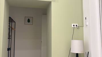 A room with a flat-screen TV mounted on the wall, a wooden bedside table with a lamp, and a power outlet on the wall.