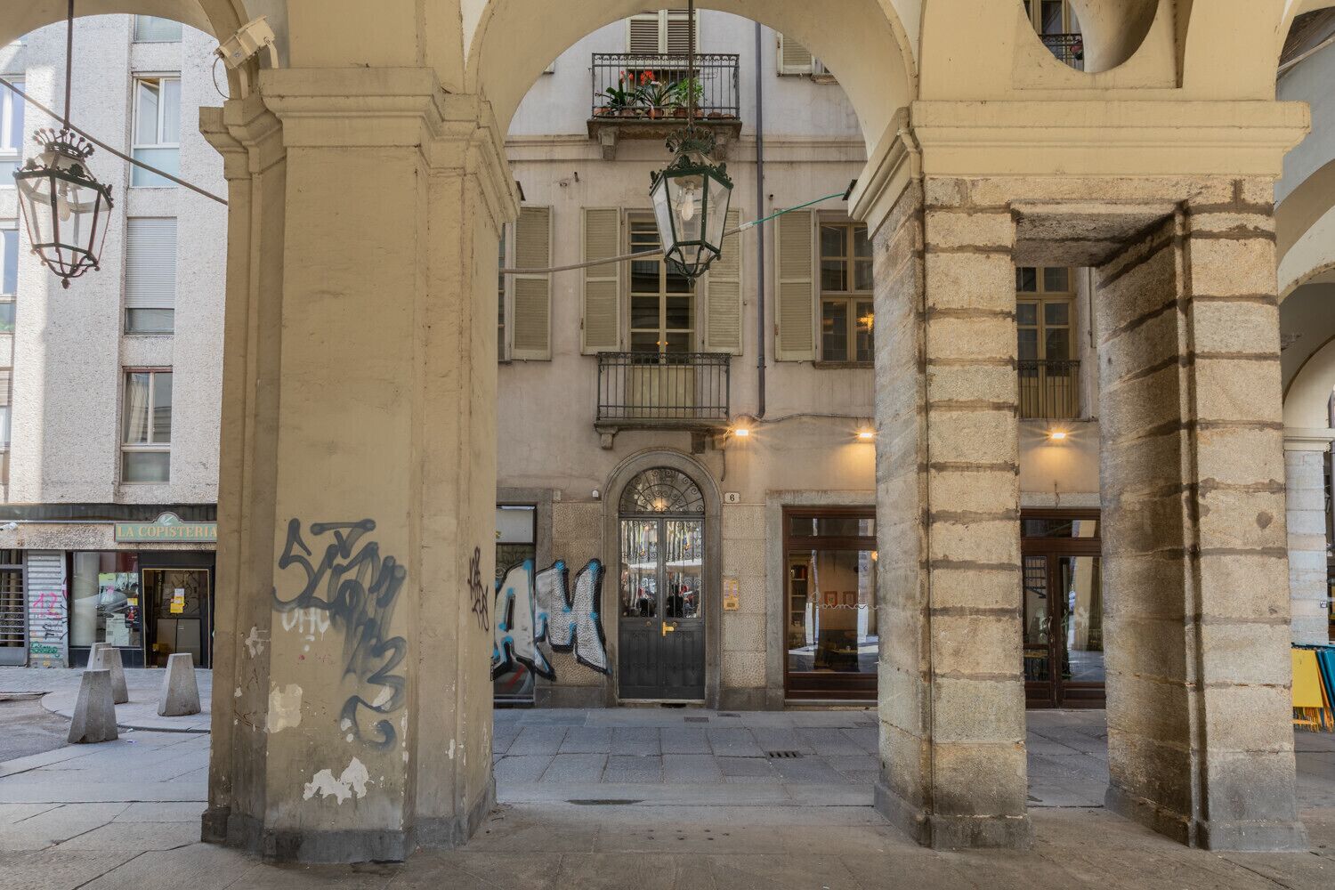 An urban street scene with a building facade, a door with graffiti, and hanging street lamps.