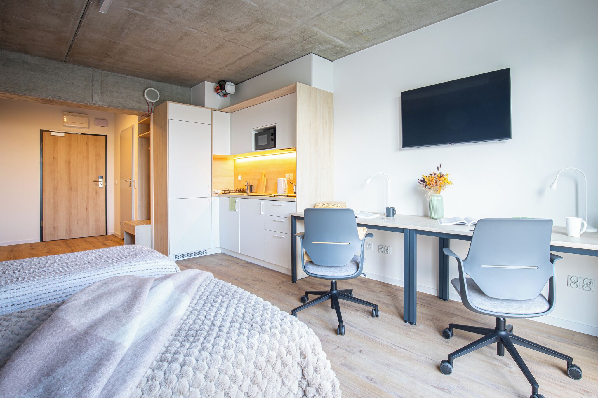 Une chambre d’hôtel moderne équipée d’un lit, d’un bureau avec deux chaises, d’une télévision et d’une kitchenette.