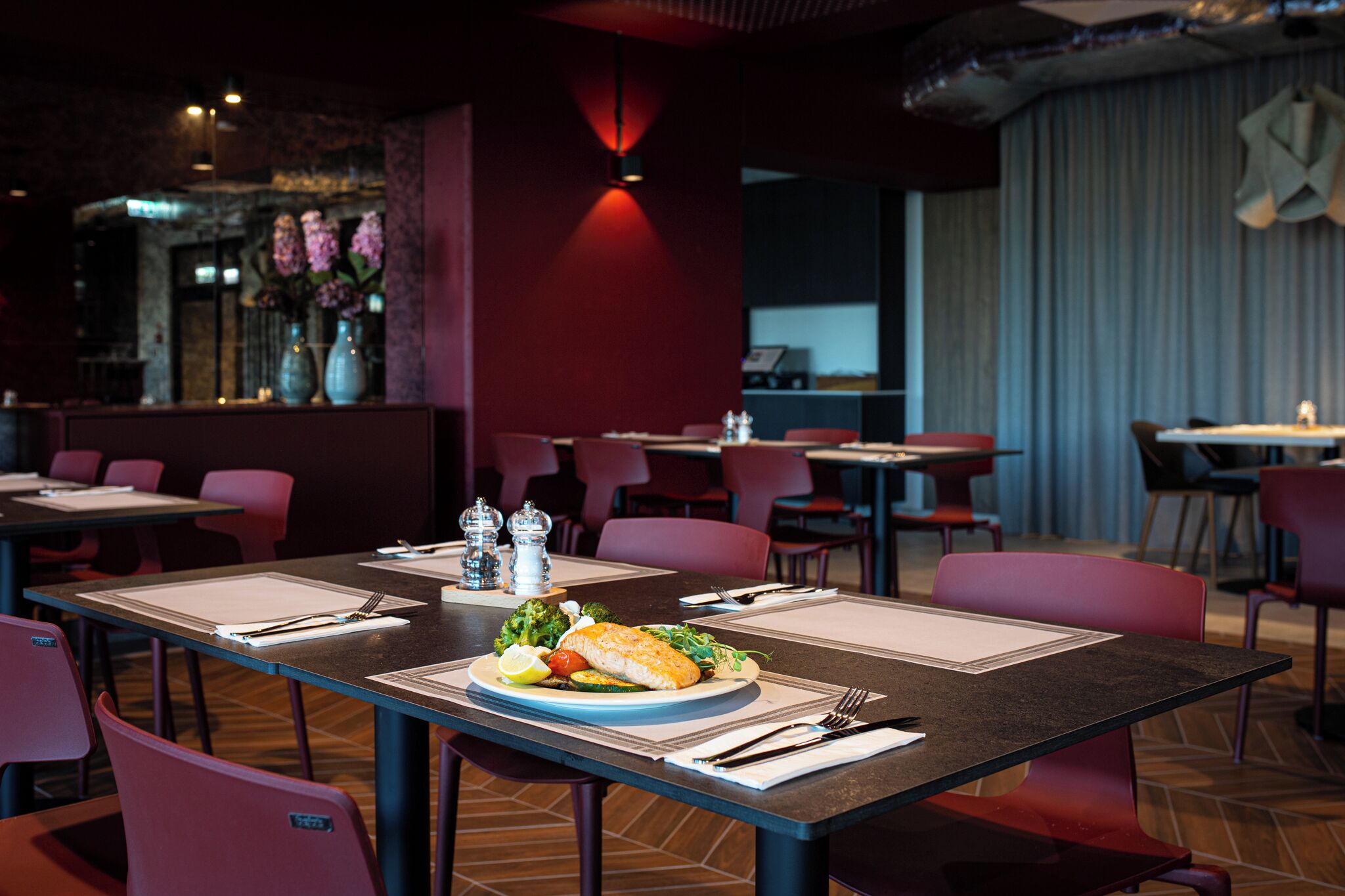 A restaurant with tables set for dining, chairs, and a decorative vase with flowers.