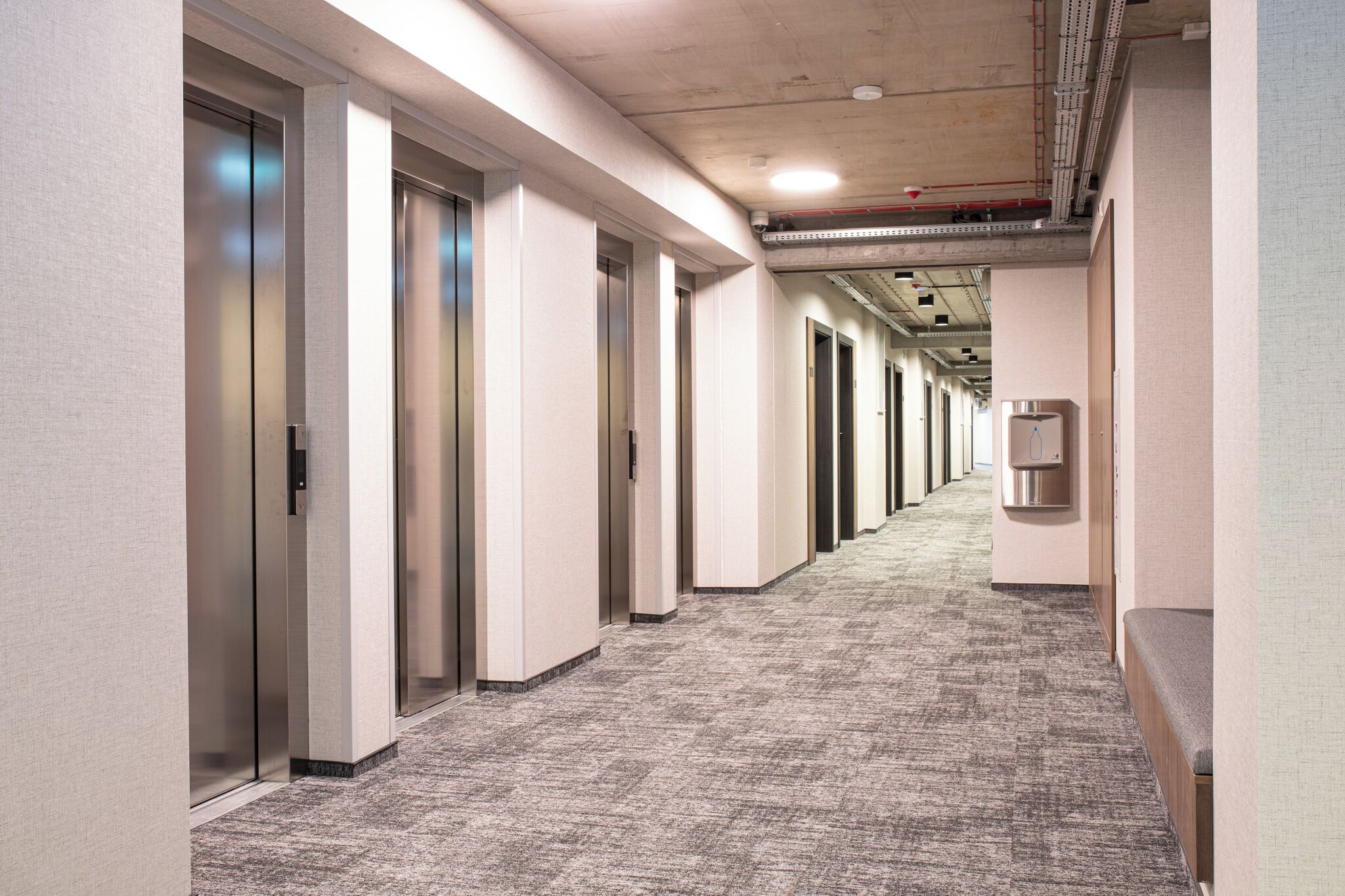 A long, narrow hallway with elevator doors on one side and a wall-mounted intercom on the other.
