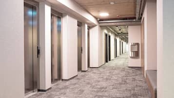 A long, narrow hallway with elevator doors on one side and a wall-mounted intercom on the other.