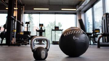 Una kettlebell y una pelota medicinal en un gimnasio con equipo de ejercicio y ventanas amplias.