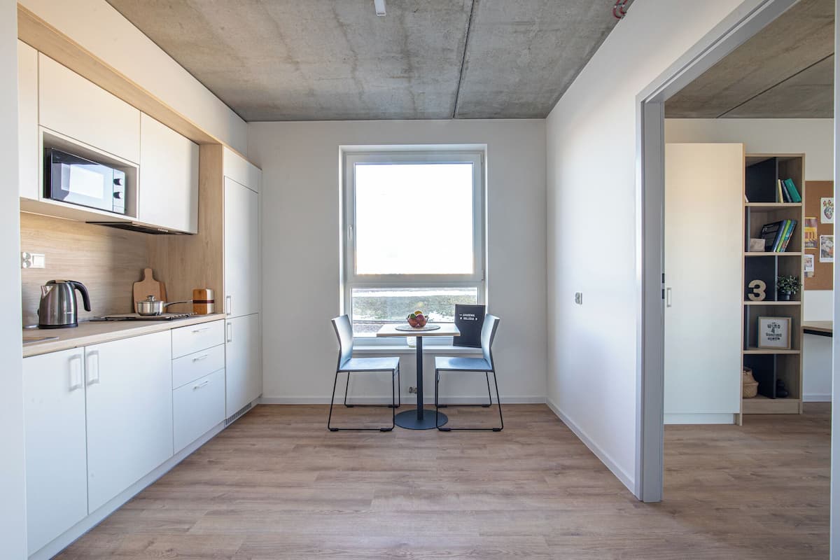 Une cuisine moderne avec des meubles blancs, un four à micro-ondes et un coin repas comprenant deux chaises et une table.