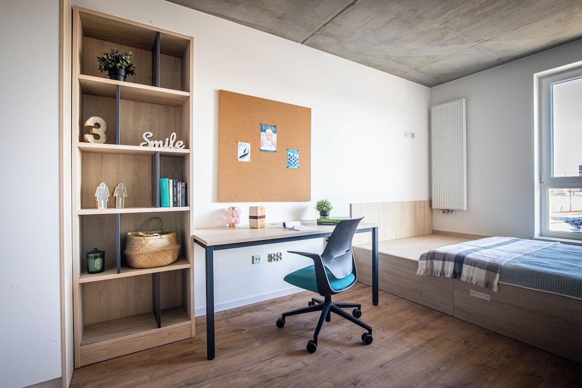 Une chambre moderne équipée d’un bureau, d’une bibliothèque, d’un tableau d’affichage en liège et d’un lit.
