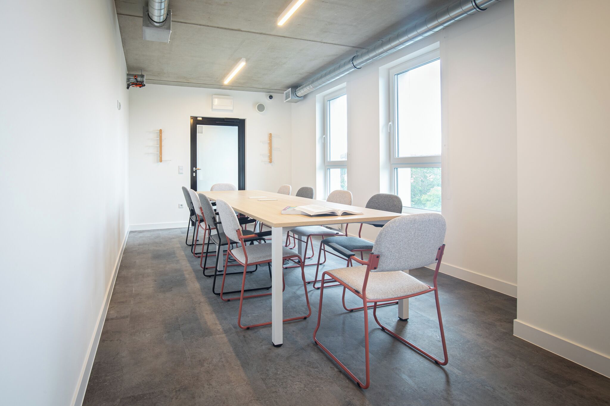 Un salón de conferencias con una larga mesa y sillas, ventanas amplias y una puerta.