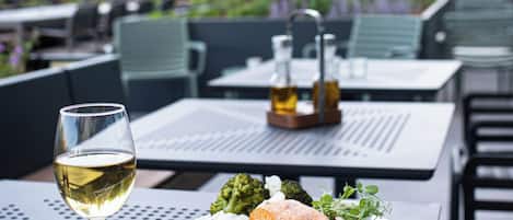 An outdoor dining table with a plate of food, a glass of white wine, and a napkin.