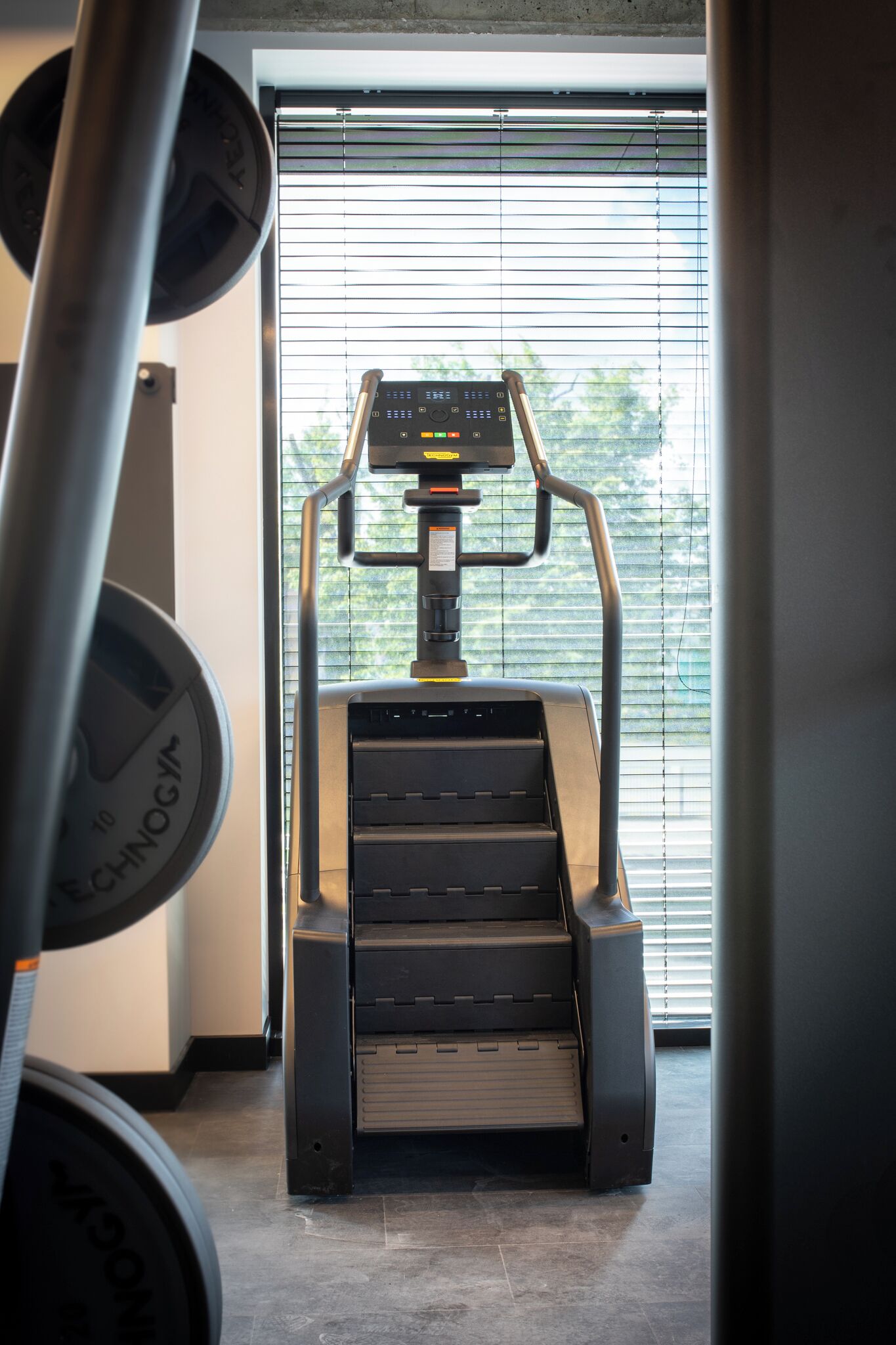 A treadmill in a gym with a window and blinds in the background.