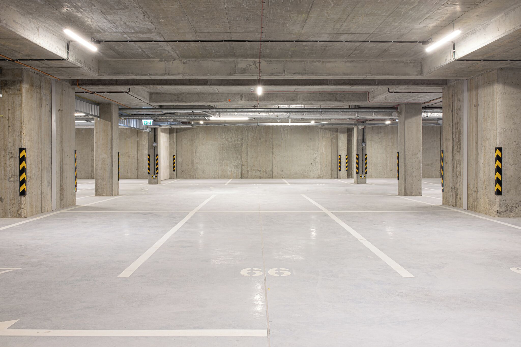 Un vaste garage souterrain avec des piliers en béton et des marquages blancs délimitant les places de stationnement.