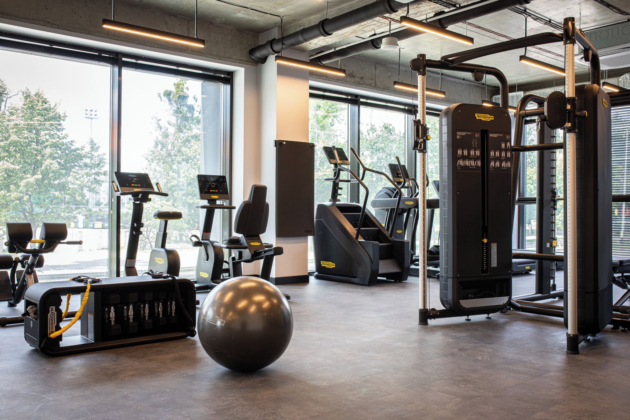 A gym with exercise equipment, large windows, and a concrete ceiling.