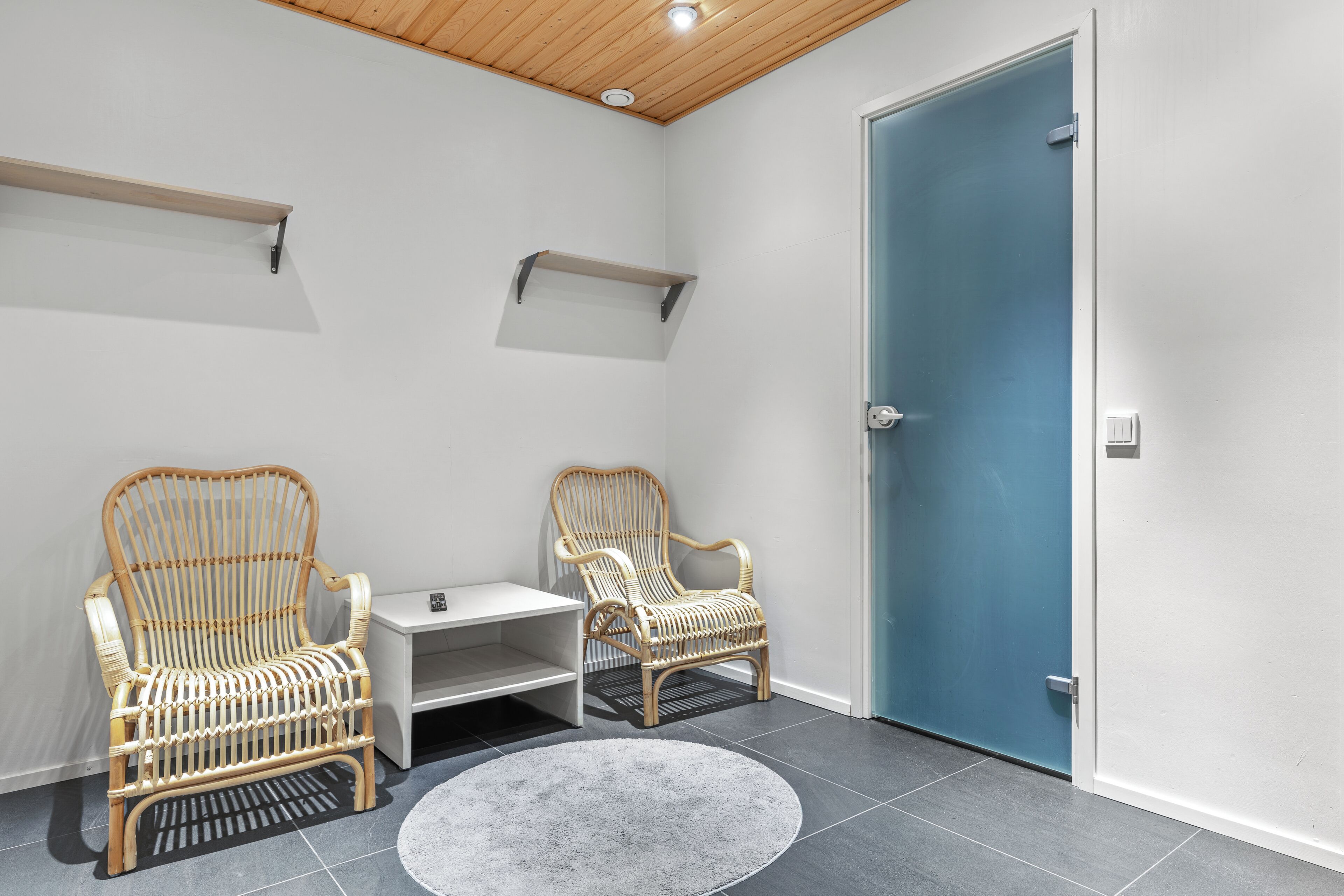 A room with two wicker chairs, a small white table, a blue door, and a grey rug.