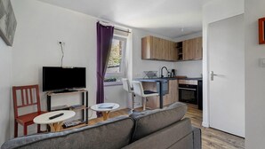 A compact living space with a sofa, a television, a small dining table, a kitchen area, and a window with curtains. - Apartment "Aurore" with Wi-Fi in Cancale, 1st Floor (Cancale)