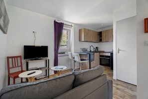 A compact living space with a sofa, a television, a small dining table, a kitchen area, and a window with curtains. - Apartment "Aurore" with Wi-Fi in Cancale, 1st Floor (Cancale)