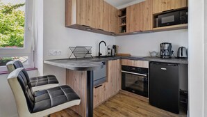 A compact kitchen with wooden cabinets, a built-in oven, a dishwasher, and a window with a view of greenery. - Apartment "Aurore" with Wi-Fi in Cancale, 1st Floor (Cancale)