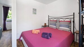 A single bed with a metal frame, a red bedspread, and two pillows with striped patterns. - Apartment "Aurore" with Wi-Fi in Cancale, 1st Floor (Cancale)
