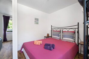 A single bed with a metal frame, a red bedspread, and two pillows with striped patterns. - Apartment "Aurore" with Wi-Fi in Cancale, 1st Floor (Cancale)