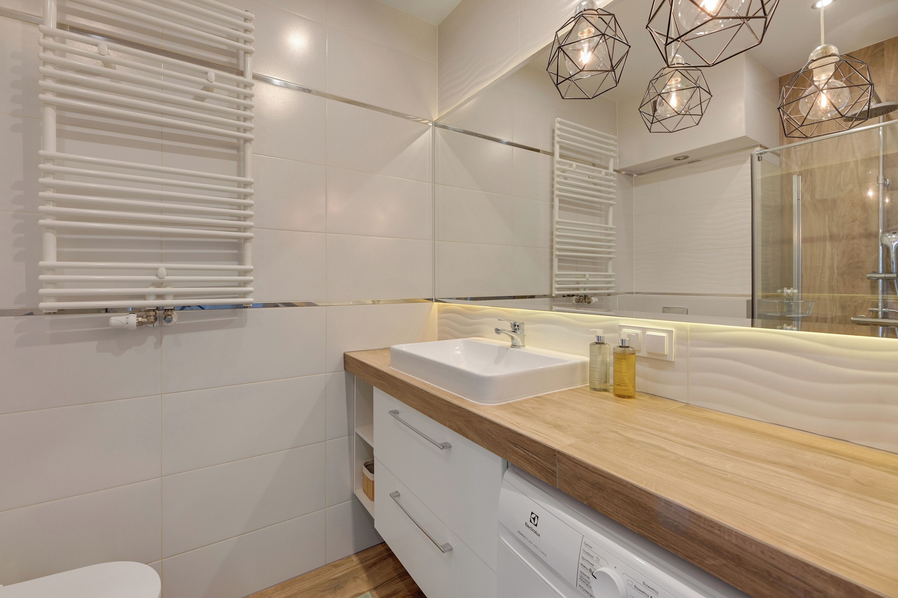 Un baño moderno con un lavamanos blanco, encimera de madera y un espejo grande.