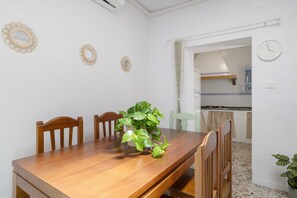 A dining area with a wooden table, chairs, a potted plant, and a kitchen in the background.