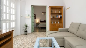 Una habitación con un sofá, un armario de madera, una mesa de centro de vidrio, una planta en maceta y una puerta que da a otra habitación.