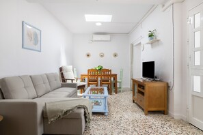 Ein Wohnzimmer mit einer Couch, einem Couchtisch, einer TV-Konsole und einem Essbereich mit Stühlen und einem Tisch.