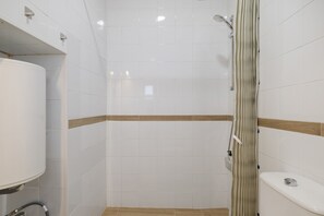 Ein Badezimmer mit weißen Fliesen, einer Dusche, einer Toilette und einem Waschbecken.