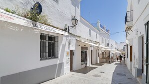 Una calle estrecha con edificios blancos, un bar llamado 'BAR EL CAPRICHO' y un cielo azul despejado.