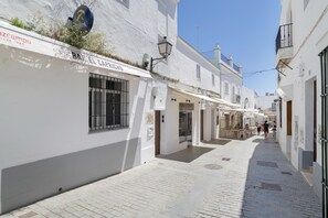 A narrow street with white buildings, a bar named 'BAR EL CAPRICHO,' and a clear blue sky.