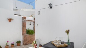 Un pequeño patio con una mesa, sillas, plantas en macetas y un muro de ladrillo.
