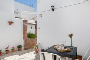 A small patio with a table, chairs, potted plants, and a brick wall.