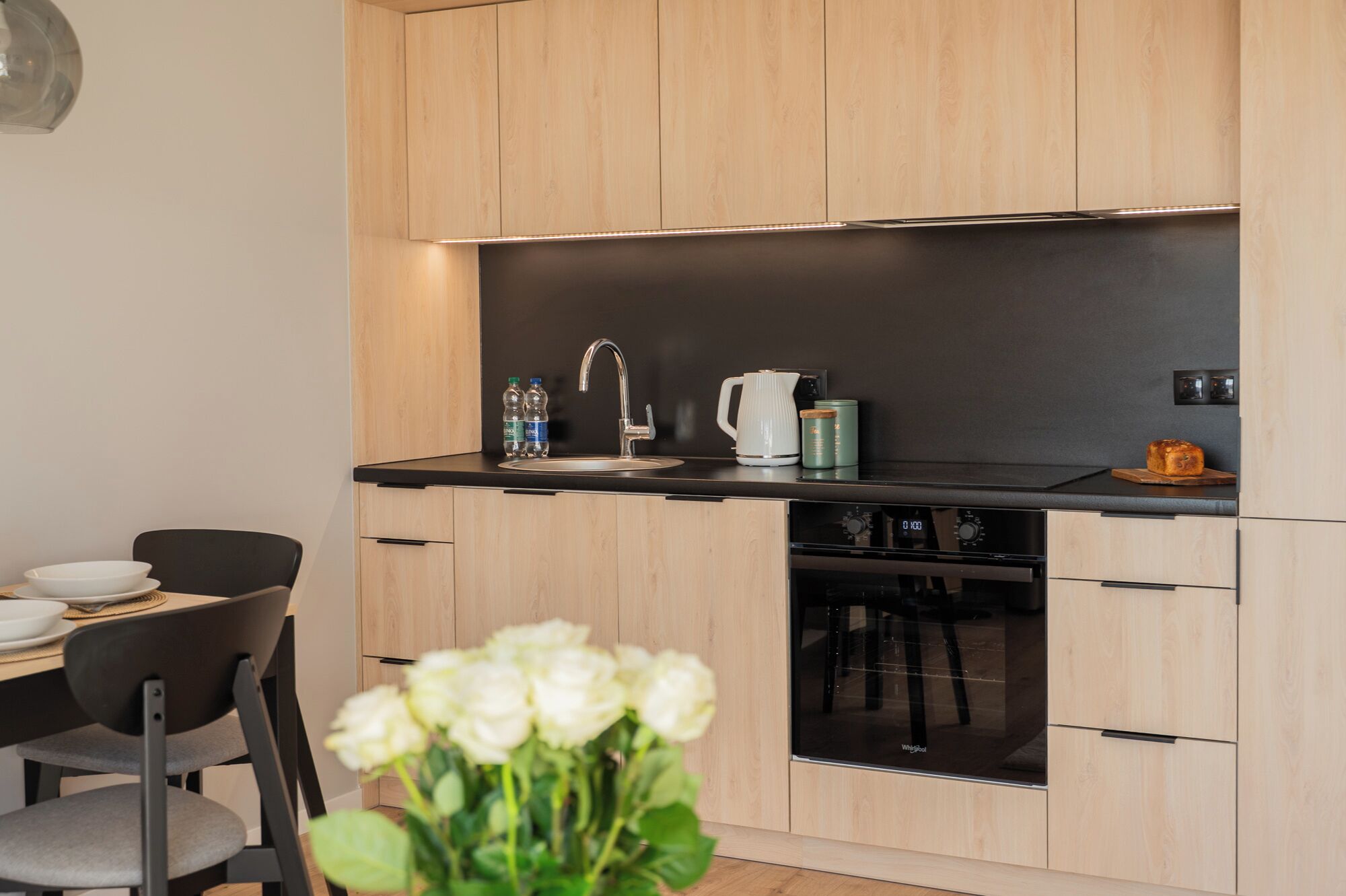 A modern kitchen with wooden cabinets, a black countertop, a sink, a coffee maker, and a dishwasher.
