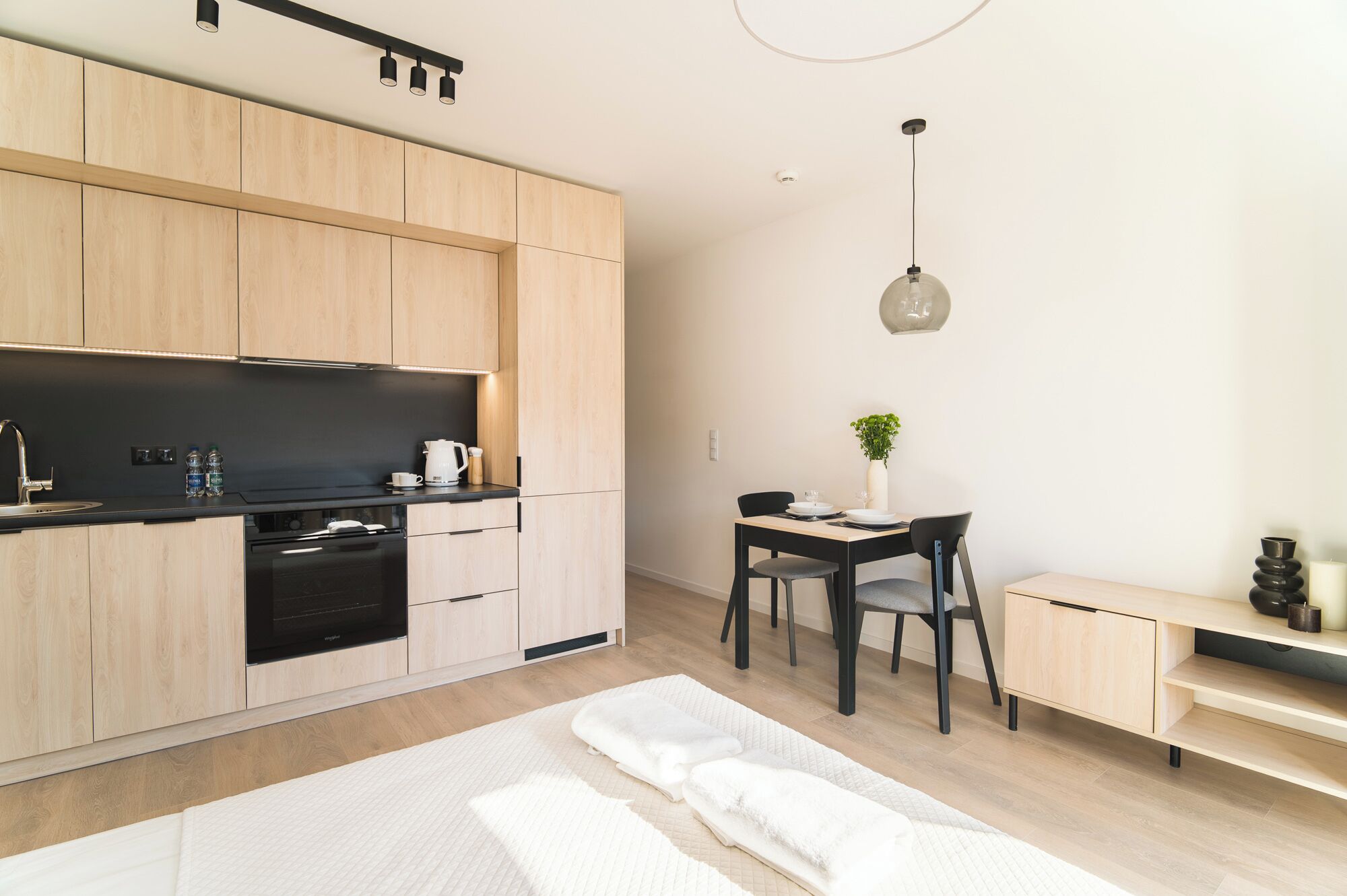 Une cuisine moderne avec des meubles en bois, un plan de travail noir et un four encastré. On y trouve également un coin repas avec une table, des chaises et un vase avec une plante.