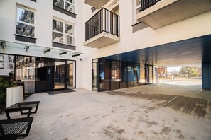 Un bâtiment moderne doté de portes vitrées, d’un espace extérieur couvert et d’une cour avec des bancs.