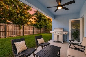 Eine Terrasse mit Gartenmöbeln, einem Grill und einem Deckenventilator.
