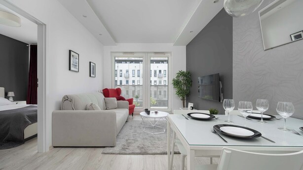 Een moderne woonkamer met een bank, een eettafel gedekt voor twee personen en een groot raam met uitzicht op de stad.