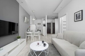 Un salon moderne doté d’un téléviseur à écran plat, d’un canapé blanc, d’une table basse ronde et d’un coin repas avec une table et des chaises blanches.