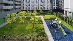 Een binnenplaats met een speeltuin, een groen gazon en een gebouw met balkons.