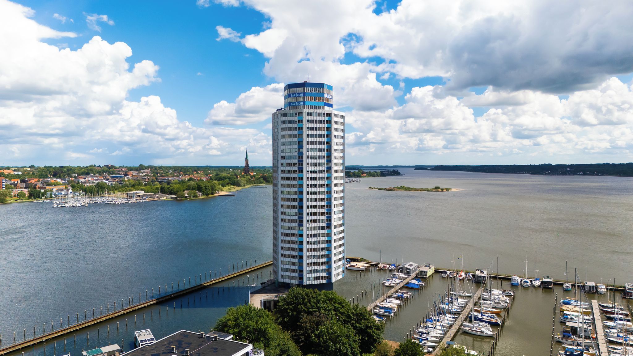 A tall building with a cylindrical shape, a marina with boats, and a river.