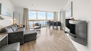 A modern living room with a sofa, a coffee table, a fireplace, and a dining area with chairs. - Modern apartment with exceptional sea view and balcony at Marina Wendtorf (Wendtorf)