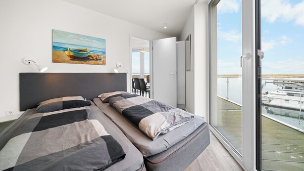 A modern bedroom with a large bed, a painting on the wall, and a balcony with a view of boats. - Modern apartment with exceptional sea view and balcony at Marina Wendtorf (Wendtorf)