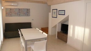 A dining area with a table and chairs, a sofa, a TV, and a staircase leading to another level. - Residence Close to the sea and the spa - Bibione (San Michele al Tagliamento)