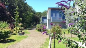 A pathway leading to a row of modern, two-story buildings with a garden in the foreground. - Residence Close to the sea and the spa - Bibione (San Michele al Tagliamento)