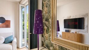 Ein modernes Wohnzimmer mit einer Couch, einer violetten Stehlampe, einem Fernseher und einem großen Spiegel, der den Raum reflektiert.