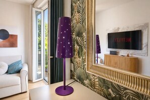 A modern living room with a sofa, a purple floor lamp, a TV, and a large mirror reflecting the room. - Elegantis Aventino Flat with Private Terrace | Colosseo & Circo Massimo (Roma)