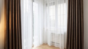 Ein Zimmer mit großem Fenster, Heizkörper und braunen Vorhängen.