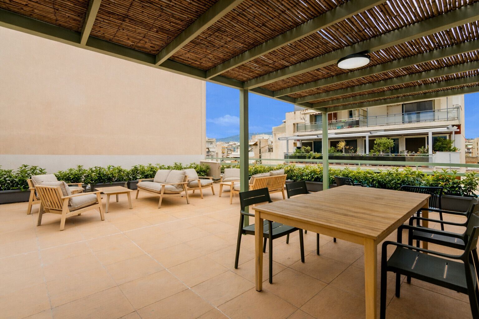 Une terrasse extérieure avec des meubles en bois, une table et une vue sur les bâtiments en arrière-plan.